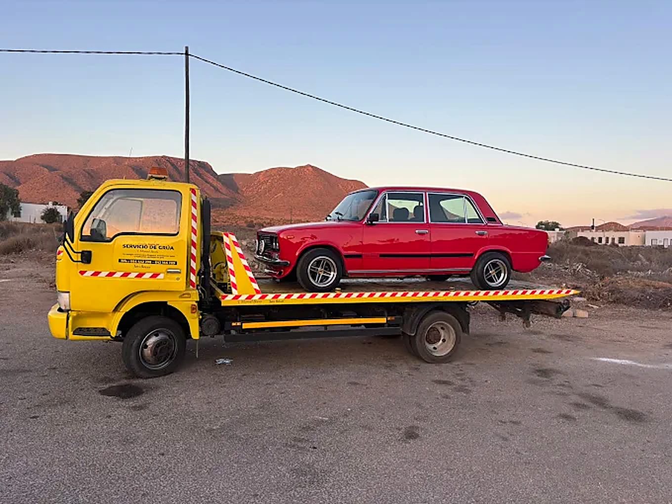 Coche clásico rojo cargado sobre la plataforma al atardecer en el campo de Níjar