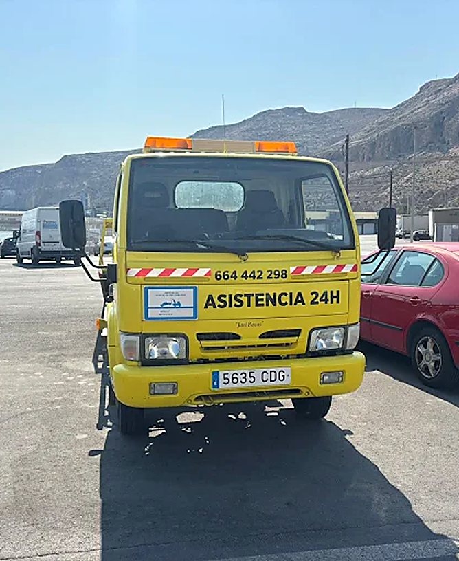 Grúa amarilla de Hermanos García con el rótulo Asistencia 24H junto a un vehículo retirado