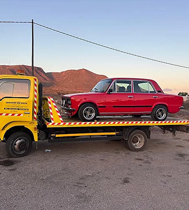 Grúa de plataforma de Hermanos García transportando un coche en una carretera de Níjar, Almería